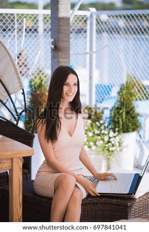 The young bewitching business-woman sits outdoor, smiles and uses laptop
