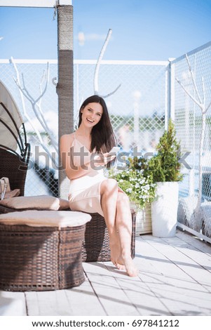 The young beautiful woman sits outdoor, smiles and keeps the phone in hand
