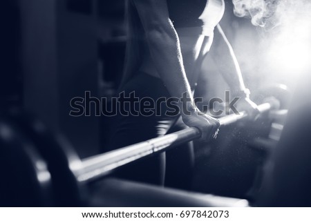 Close-up of a girl holding her hands with a barbell for pulling, squatting, fitness in the gym. Concept sports, toned picture, copyspace for text