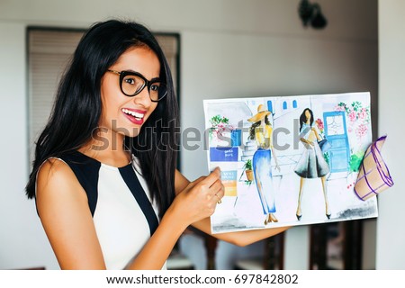 A happy young female Indian fashion designer showing her garment designs on a sheet