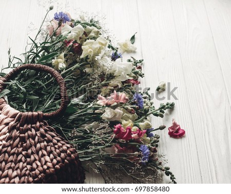 beautiful wildflowers in wicker bag on rustic white wooden background. colorful flowers in basket in light, space for text. rustic wedding concept, woman mothers day, rural summer picture