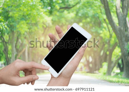 Woman hand holding and using smart phone (mobile) over blurred image of nature background.