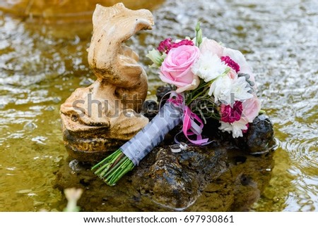 Close up of two golden wedding rings and  beautiful fresh wedding bouquet of pink and white roses on stone in water, free space. Wedding details outdoor with copy space