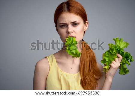 Woman eating lettuce leaves on gray background                               