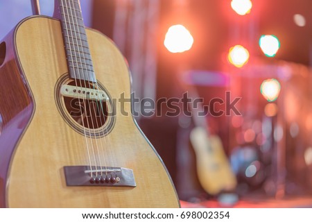 Close up yellow acoustic guitar on a stand in front of a stage set up for an upcoming concert. Royalty-Free Stock Photo #698002354