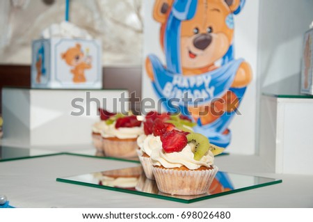 Birthday composition. Three cupcakes with white butter cream and slices of strawberry, kiwi on celebration pictures background