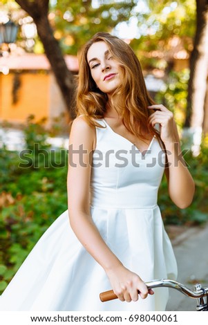 Attractive girl in a white dress walking around the city with an yellow bike
