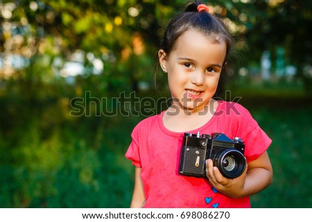 Portrait of young beautiful child with retro camera. Little girl with old photography camera in hands outdoors.
