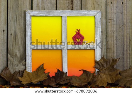 Rustic window with blank colorful window panes with red house with heart and the word Family by fall leaves border with aged wood background; seasonal, home and nature background with copy space