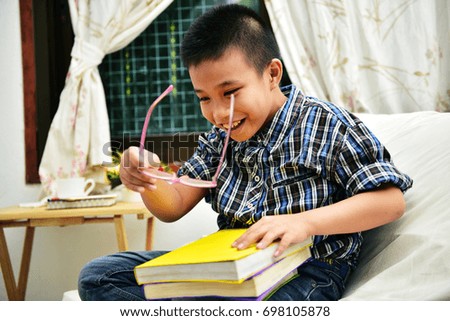 A funny young boy play with glasses with many book at home in selective focus.