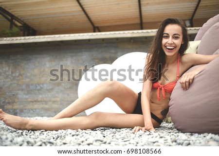 Cheerful laughing yong woman lies on the rocks on the beach near bean bags