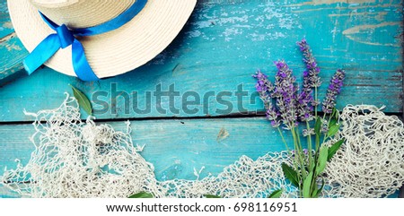 Summer time sea vacation background with straw hat, vintage fishing net and lavender bouquet on weathered wood blue background with copy space. Mono colour concept. Vintage toning, wide photo.