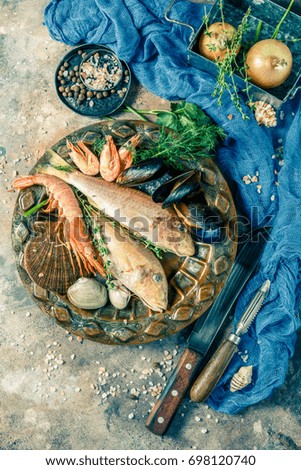 Photo of fish, shrimp, clams on plate attable with blue cloth, spices