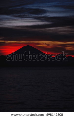 Bright tropical sunset and silhouettes of Agung volcano on the island of Bali in Indonesia. Magic colors during sunset, bright clouds and red sun light. Journey to a tropical island in the ocean.