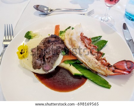 steak and lobster with colorful vegetables on white plate