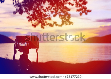 Silhouette photo of the mirrorless camera mounting on a tripod to take pictures with sea view while sunset on the beach.