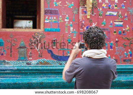 A man taking a photo on the wall of asian style building in laos with blurred asian style building backgroud 