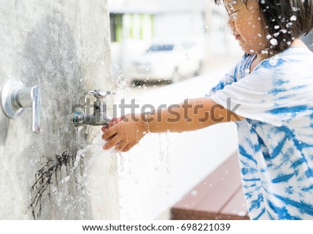 Save water and environment concept.Little asian girl hand with clear water splash.Close up young asian little girl taking water from faucet in the garden.