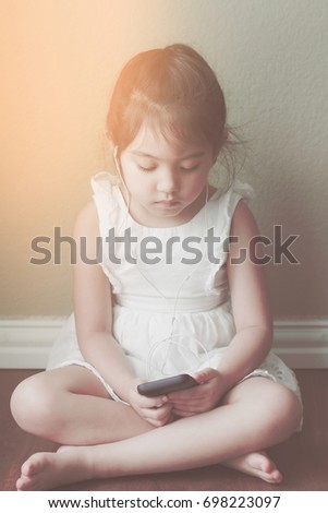 little girl sitting on wood floor alone and watching nursery rhymes  from smart phone by self, filtered tones