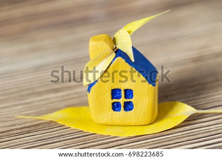 Miniature yellow toy house with bright yellow autumn leaf on the blue roof. Wooden surface. Selective focus. Autumn concept.