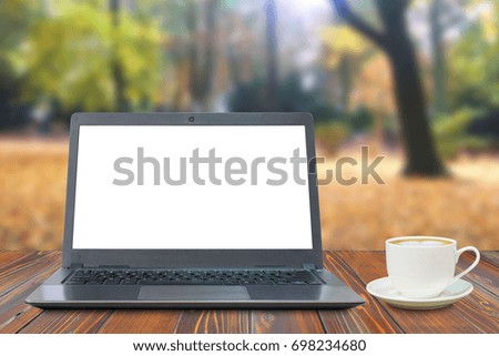 Laptop with white screen and a cup of coffee on wooden table in the park