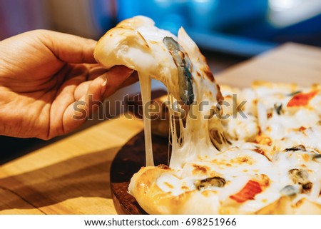 Woman holding a piece of pizza loaded with cheese looks tasty from the tray in the pizza restaurant one Sunday afternoon.