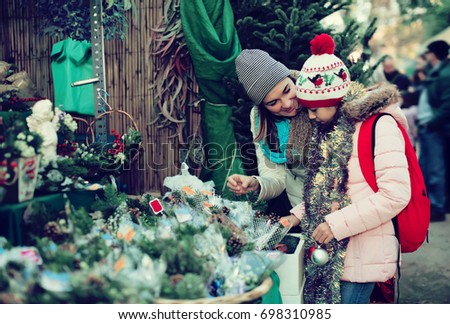 Adult mom and girl buying flowers decoration at Christmas market
