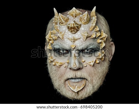 Horror and fantasy concept. Man with dragon skin and beard. Monster face with white eyes, sharp thorns and warts. Demon head isolated on black. Alien or reptilian makeup.
