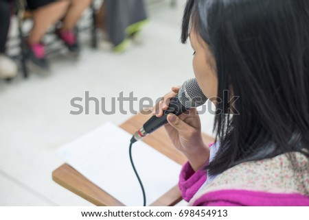 A microphone was held by a woman sitting on a desk, shot in selective focus mode, set in natural mood and atmosphere in a simple position