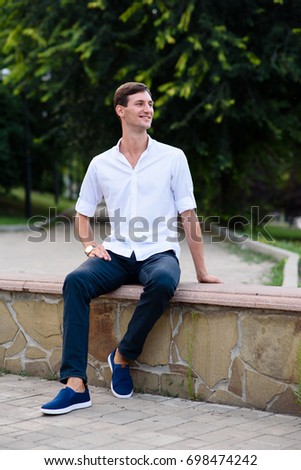 handsome guy in a white shirt smiles and rests in the park.