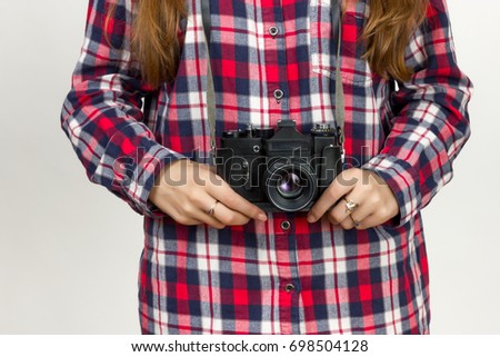 Portrait of a pretty woman  in plaid shirt holding an old camera in hands standing over gray background 