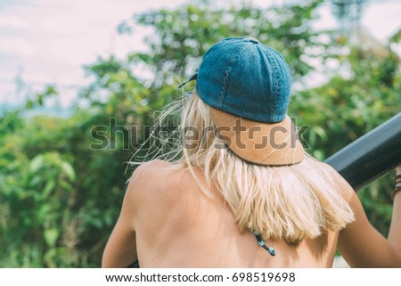 Young blonde white caucasian female in baseball hat riding in the back of the car thru jungle rainforest. Travel lifestyle background. 