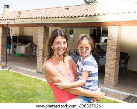 Mother and her child girl playing, kissing and hugging in front of house home