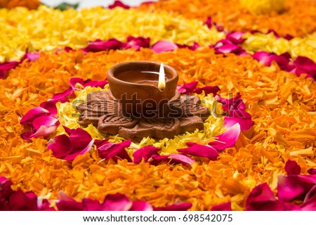 flower rangoli for Diwali or pongal made using marigold or zendu flowers and red rose petals over white background with diwali diya in the middle, selective focus
