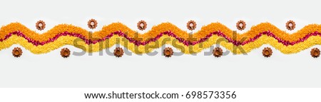 Decorative Flower rangoli Strip or Border or Pattern for Diwali or Pongal Festival made using marigold or zendu flowers and red rose petals over white background with Clay Oil Lamps, selective focus Royalty-Free Stock Photo #698573356