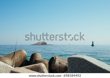 Sea horizon and an island and tetrapods.There is a fishing rod placing on a tetrapod. 