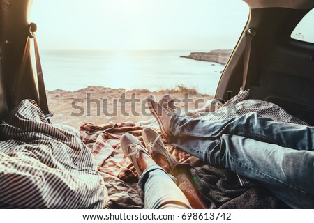 Man and woman relaxing inside trunk and watching at the sea. Fall car trip in sunset. Freedom travel concept. Autumn weekend. Royalty-Free Stock Photo #698613742
