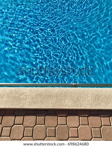Edge of swimming pool showing blue mosaic tiles, steel handrail, concrete and brick paving edge