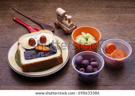 School lunch box snacks for kids over wooden background. Back to school. Healthy and fun snack option for moms. Cute food art creative concepts. Bow with fruits and vegetables and cute face sandwich.
