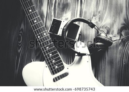 Electric guitar, pedal and headphones on wooden table. Close up. Black and white photo. Making music concept.