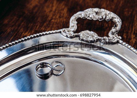 A bride and groom wedding ring on a shiney silver tray.
