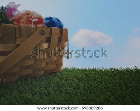 Christian Cross necklace hanging from wooden basket on grass field with sky background