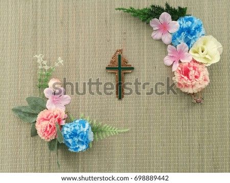 Christian Cross necklace on weaving mat with various colorful artificial flowers decoration