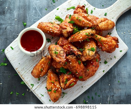 Baked chicken wings with sesame seeds and sweet chili sauce on white wooden board. Royalty-Free Stock Photo #698898115