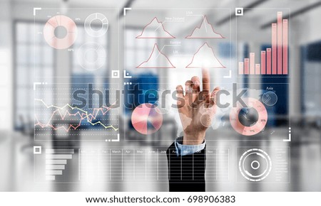 Hand of businesswoman working with media interface on screen and office interior at background