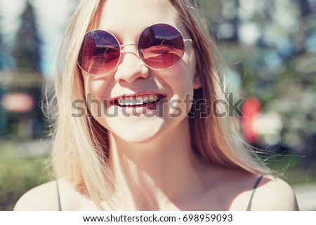 Headshot image of happy young European blond lady laughing out loud in round stylish sunglasses outdoors.Fresh & lively portrait of Caucasian student having fun with friend.Instagram filtered picture.
