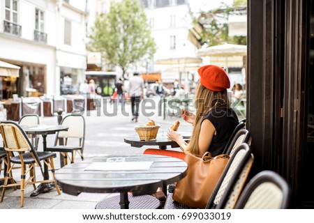 Young stylish woman in red beret having a french breakfast with coffee and croissant sitting oudoors at the cafe terrace Royalty-Free Stock Photo #699033019