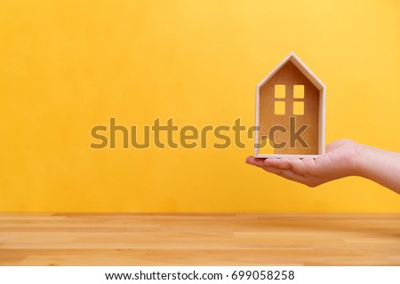 Hand holding home model with wooden table and yellow background for house ownership or real estate business concept