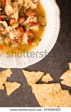 
White chicken chili with red peppers, chicken, and beans in white bowl with corn tortilla chips top view
