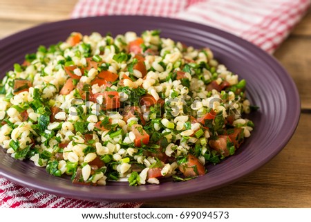 Tabbouleh salad with bulgur, tomatoes, parsley, green onion and mint in plate on wooden table. Traditional middle eastern or arab dish. Selective focus.